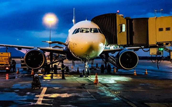 Avion de ligne stationné au contact d’une passerelle d’embarquement au crépuscule sur un tarmac mouillé