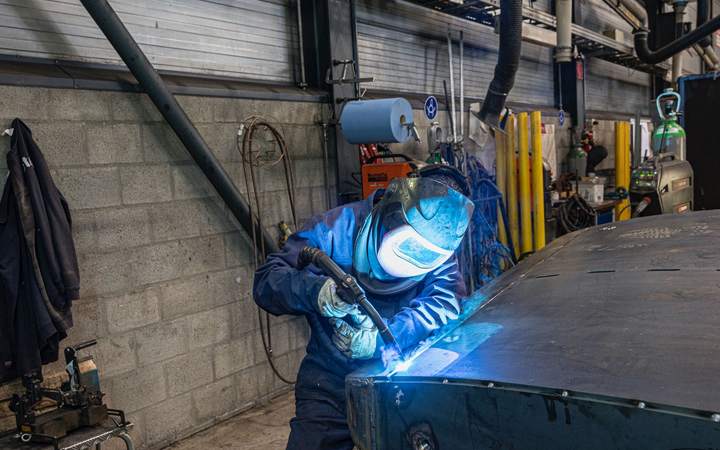 Soudeur casqué travaillant sur un élément de carrosserie dans un atelier automobile
