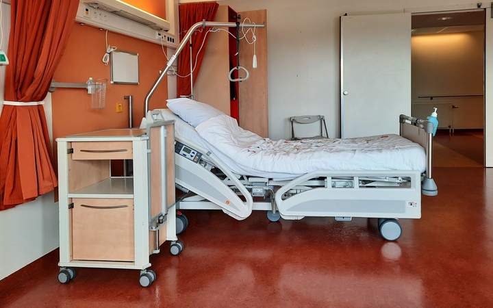 Chambre d’hôpital avec lit médicalisé, table de chevet et rideau orange