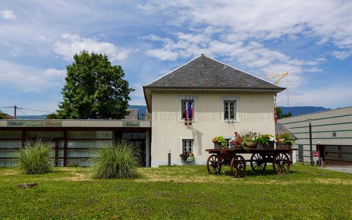 Petite mairie au toit d’ardoise pavoisée du drapeau français, avec charrette fleurie