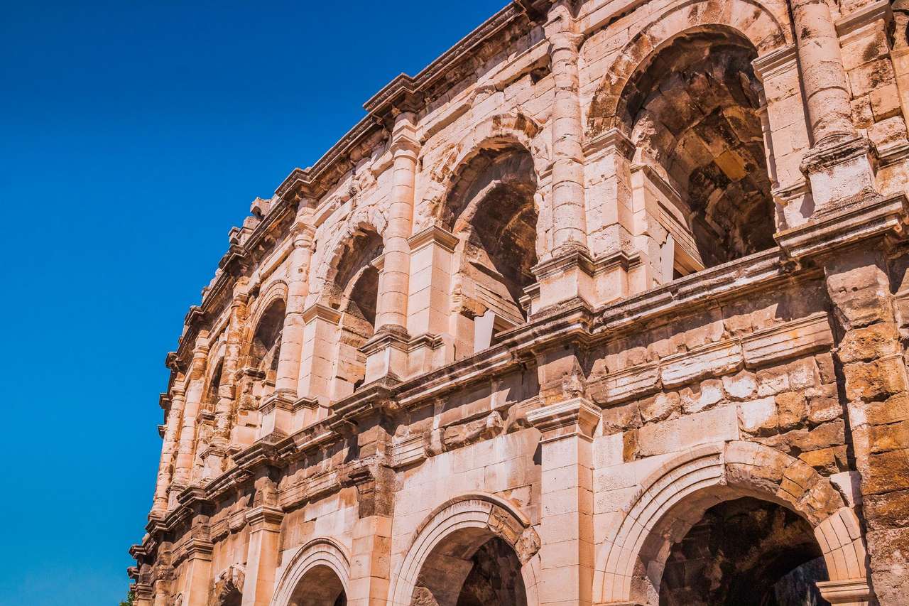 Façade à arcades et pilastres des arènes romaines de Nîmes, sous un ciel bleu