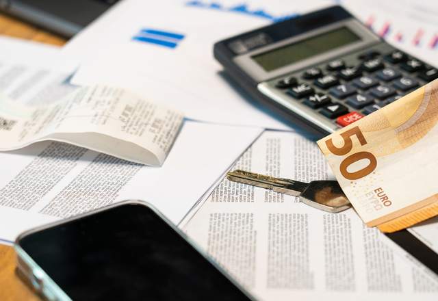 Calculatrice, billets en euros et documents imprimés étalés sur une table de travail