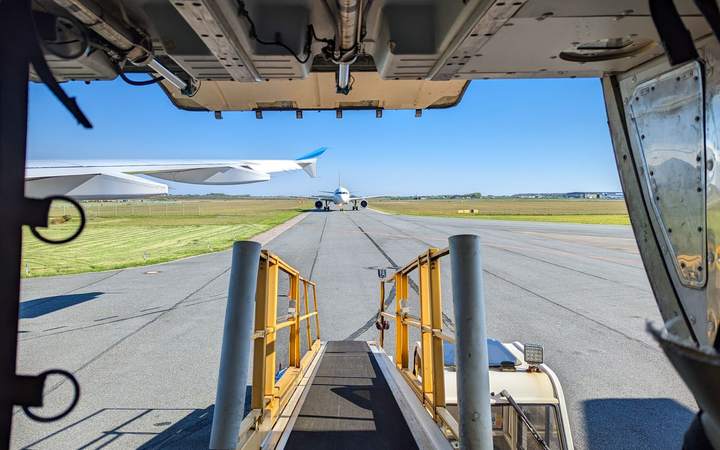 Rampe d’accès vue depuis la porte cargo d’un avion, avec un appareil sur la piste