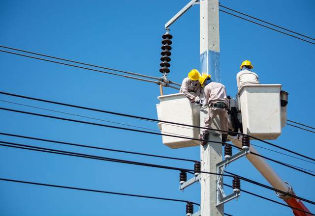 Deux techniciens casqués dans une nacelle intervenant sur une ligne électrique aérienne sous ciel bleu