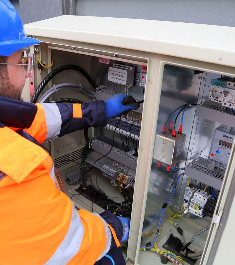 Électricien casqué en tenue haute visibilité intervenant sur une armoire électrique extérieure ouverte