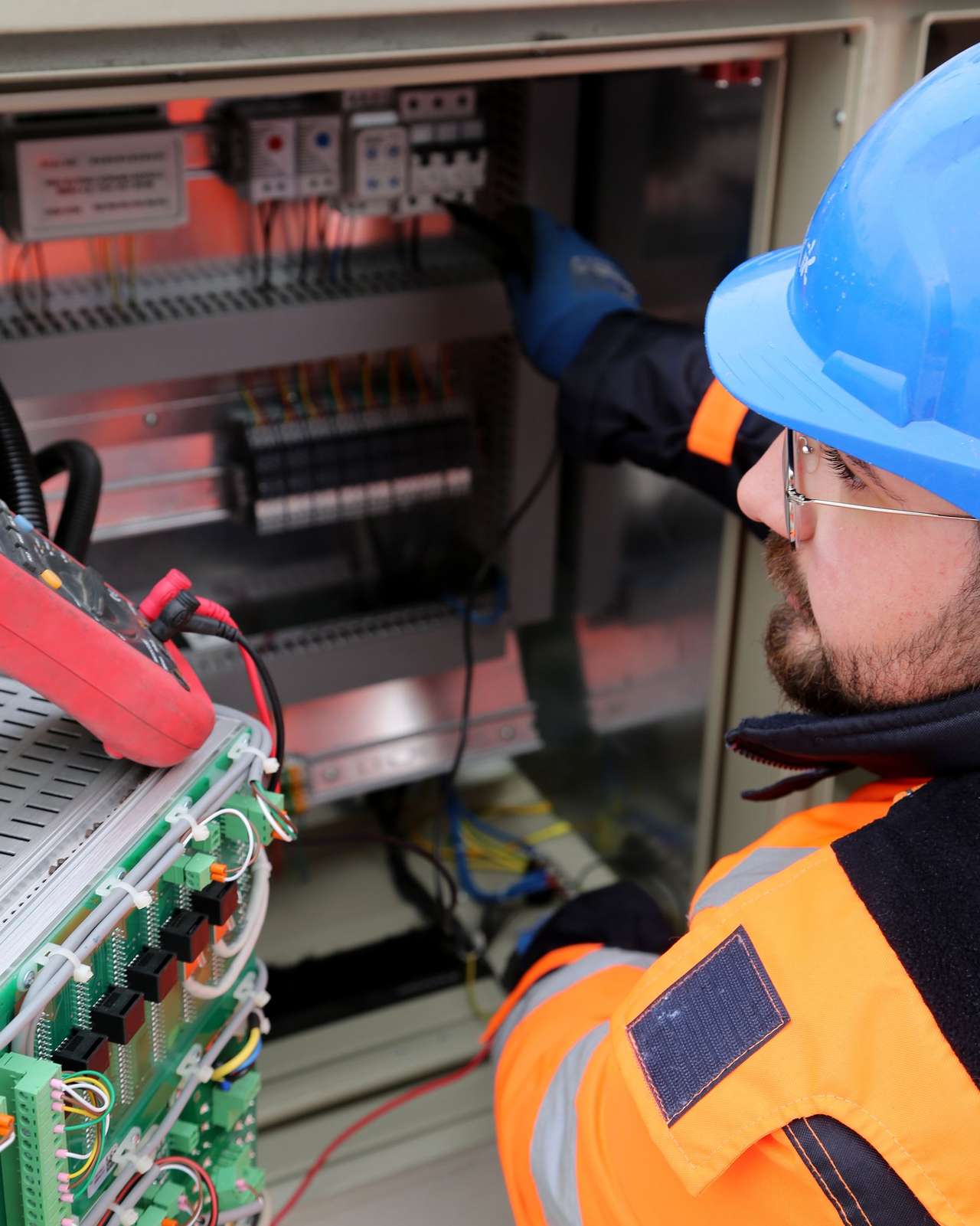 Électricien en tenue de chantier réalisant une mesure à la pince dans un coffret