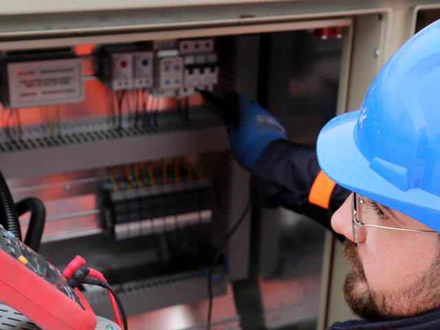 Électricien en tenue de chantier réalisant une mesure à la pince dans un coffret