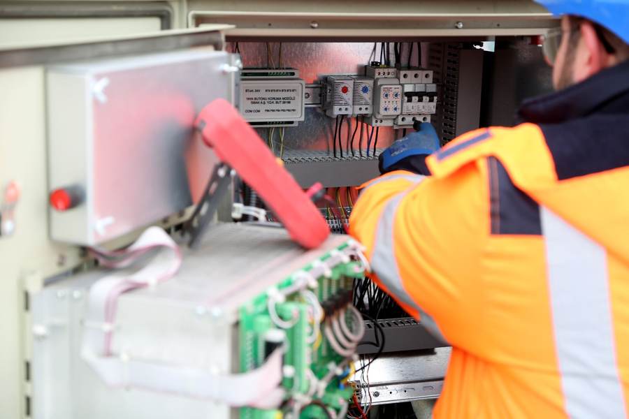 Technicien en veste haute visibilité effectuant une mesure à la pince ampèremétrique dans une armoire électrique