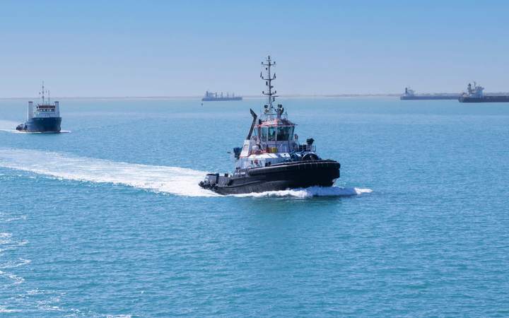 Remorqueur filant à vive allure en mer vers des navires au mouillage