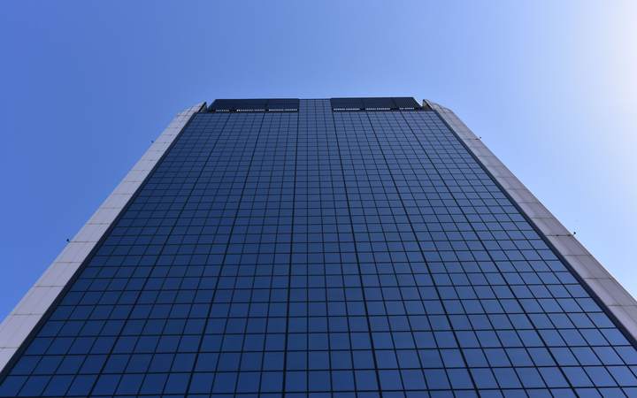 Façade vitrée d’une tour de bureaux vue en contre-plongée sous un ciel bleu