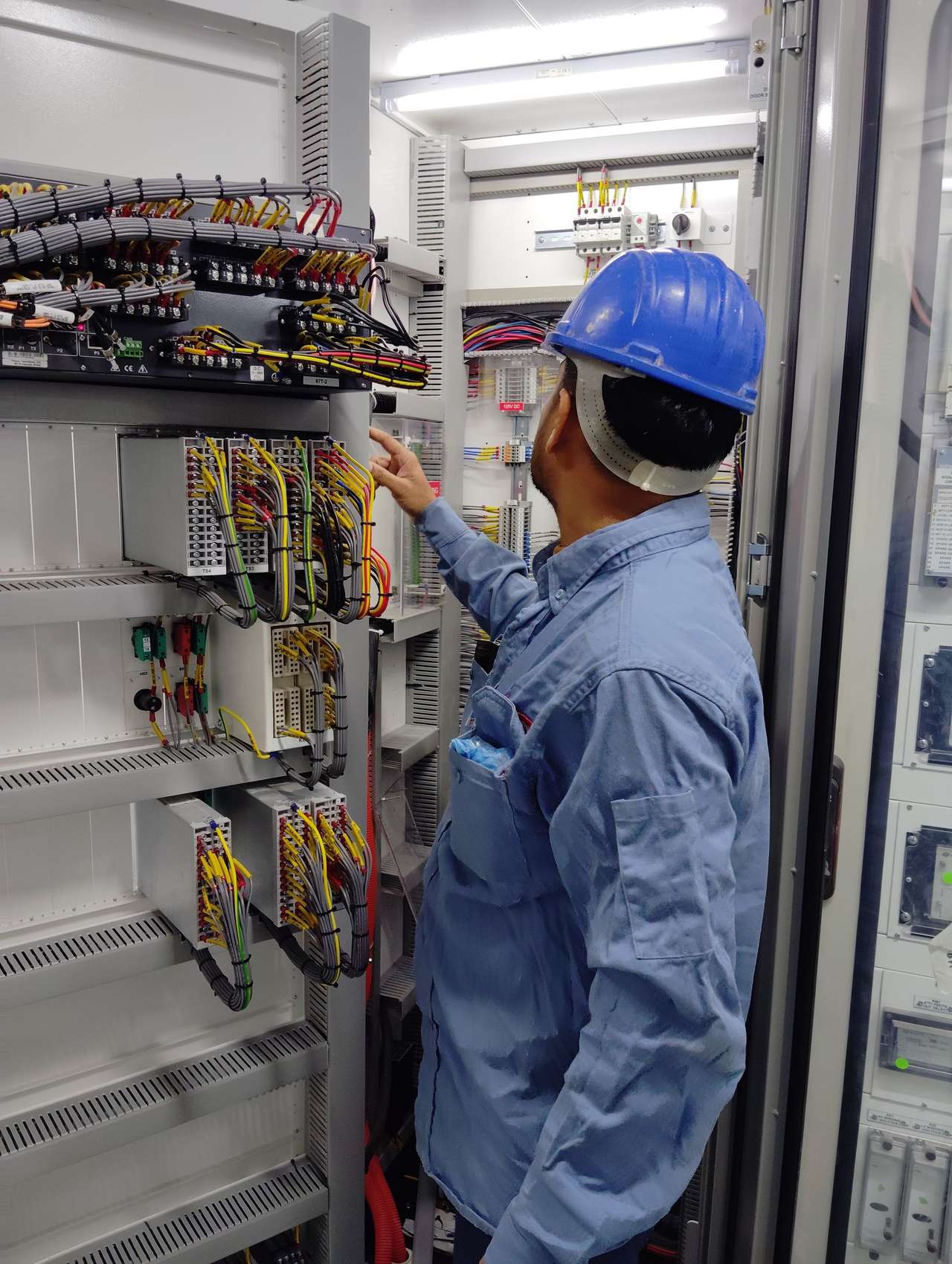 Technicien casqué examinant le câblage d’une armoire de protection et de commande