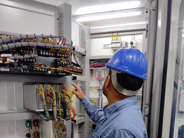 Technicien casqué examinant le câblage d’une armoire de protection et de commande