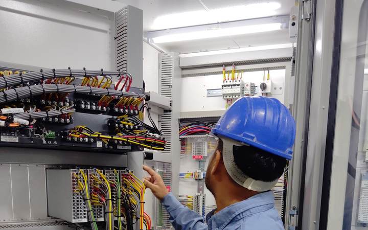 Technicien casqué examinant le câblage d’une armoire de protection et de commande