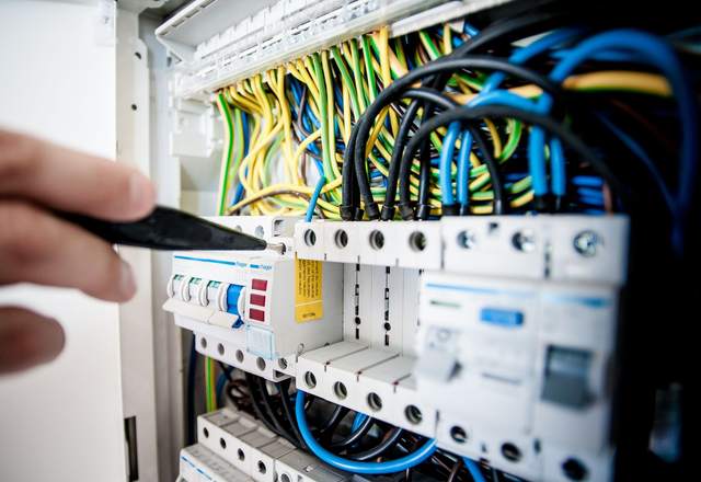 Main tenant un tournevis devant un tableau électrique modulaire avec disjoncteurs et câblage coloré