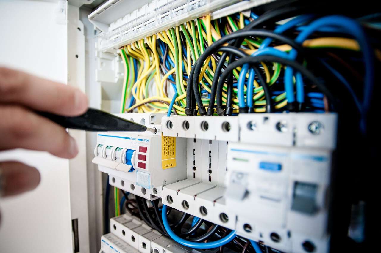 Main tenant un tournevis devant un tableau électrique modulaire avec disjoncteurs et câblage coloré