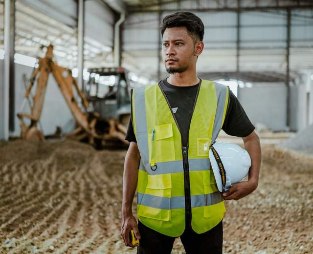 Ouvrier en gilet haute visibilité, casque à la main, dans un hangar industriel