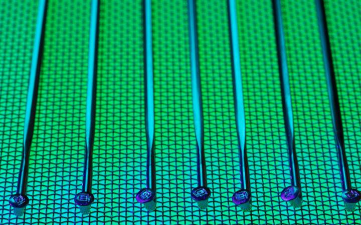 Pointes de test alignées au-dessus d’une plaquette de silicium à motifs, sous éclairage vert