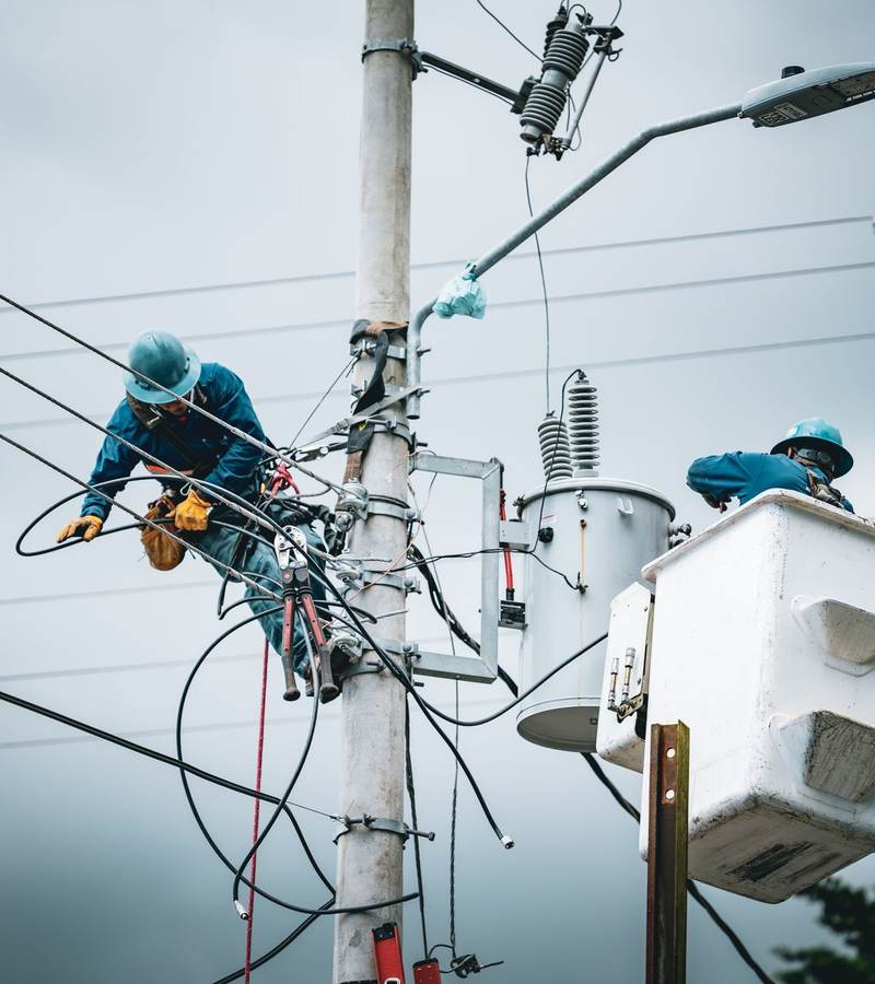 Techniciens casqués intervenant sur un poteau de réseau électrique depuis une nacelle