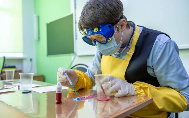 Chercheuse équipée de lunettes, masque et gants manipulant des réactifs dans un laboratoire de chimie