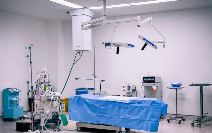 Bloc opératoire vide avec table recouverte d’un champ bleu, scialytiques et appareil d’anesthésie