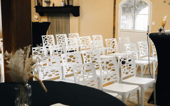 Salle de réunion aménagée en rangées de chaises blanches sous des poutres apparentes