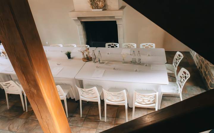 Salle de réunion lumineuse avec longue table blanche et chaises, poutre en bois au premier plan