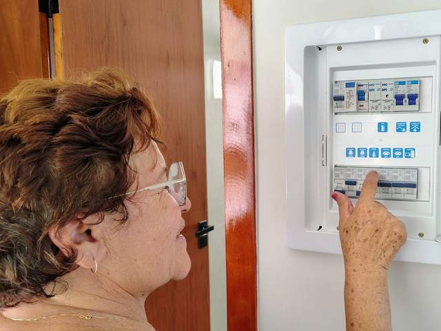 Femme de profil manipulant un disjoncteur dans un tableau électrique domestique ouvert