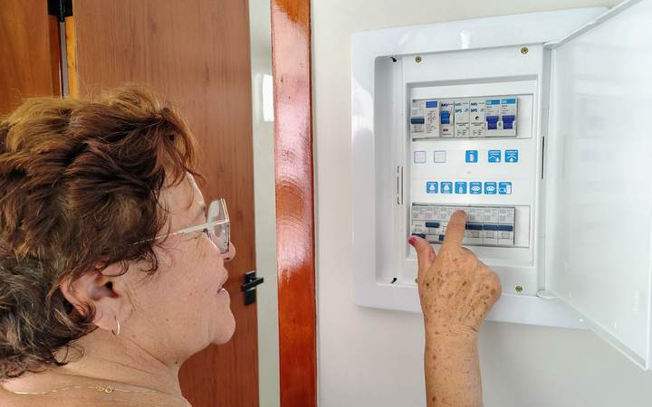 Femme de profil manipulant un disjoncteur dans un tableau électrique domestique ouvert