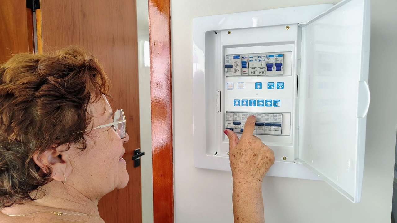 Femme de profil manipulant un disjoncteur dans un tableau électrique domestique ouvert