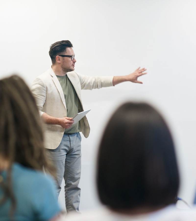 Formateur désignant un tableau blanc devant des stagiaires assis vus de dos