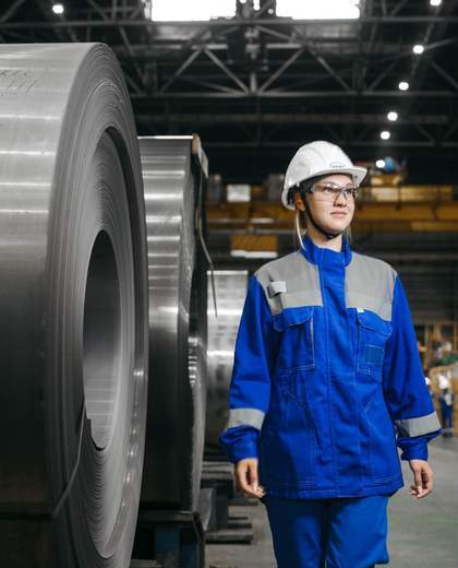 Technicienne casquée en tenue de travail dans un hall de production de bobines d’acier