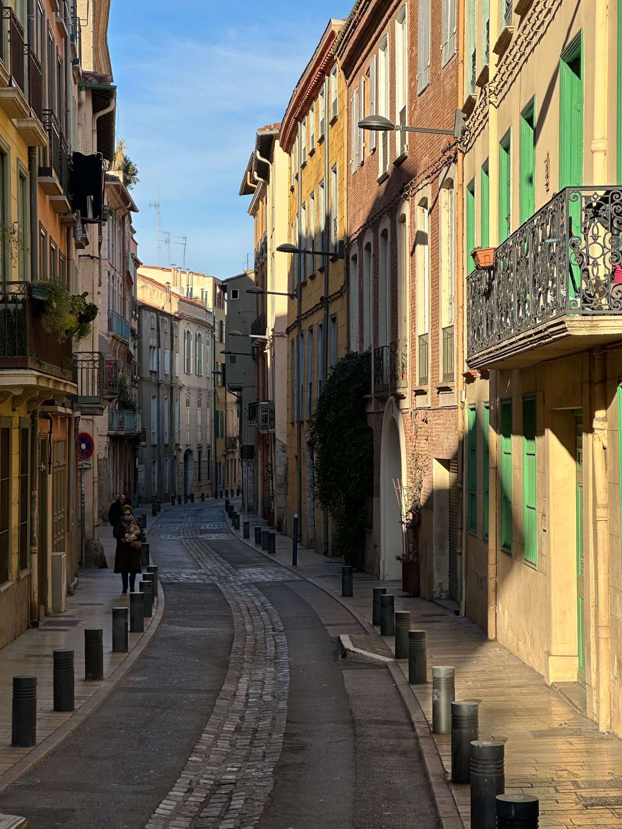 Rue étroite du centre de Perpignan, bordée de façades colorées, de balcons en fer forgé et de bornes