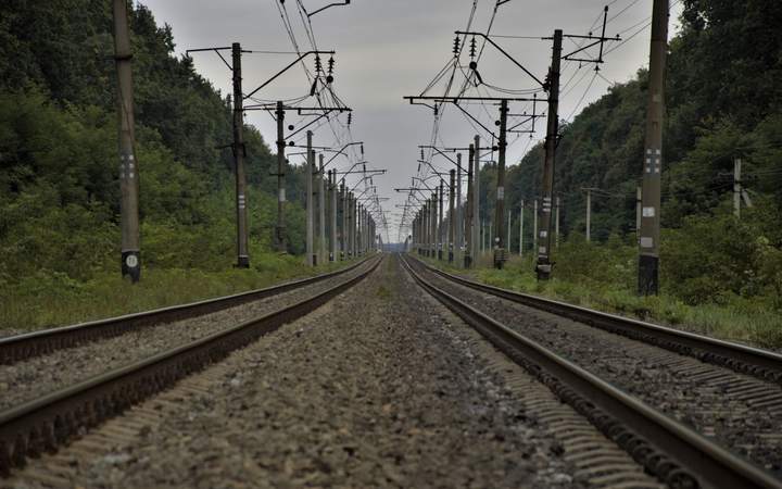 Voies ferrées électrifiées avec poteaux et fils de caténaire traversant une vallée boisée