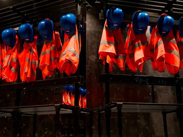 Casques bleus et vestes orange haute visibilité suspendus sur des portants dans un vestiaire