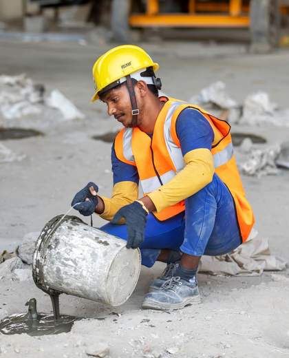 Ouvrier casqué en gilet haute visibilité versant du mortier sur un chantier