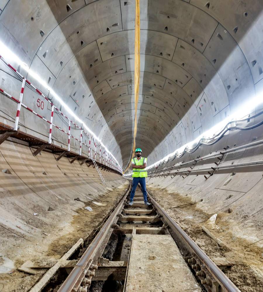 Ouvrier en gilet haute visibilité et casque debout sur la voie au centre d’un tunnel en voussoirs éclairé