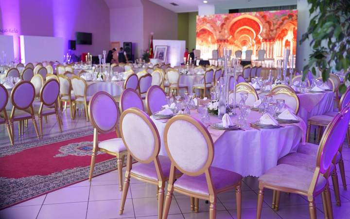 Salle de réception dressée pour un banquet avec tables rondes et chaises dorées