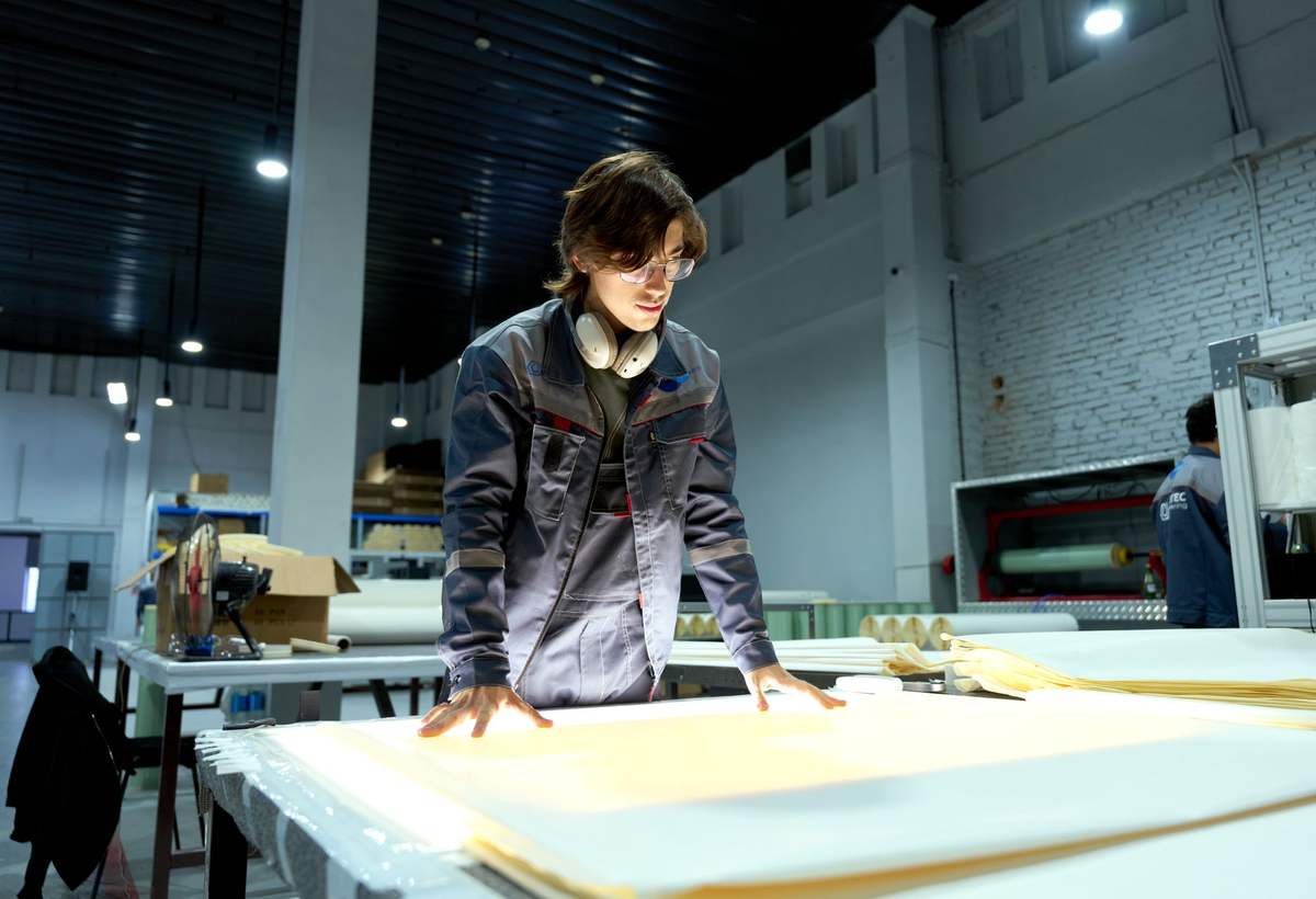 Opérateur en veste de travail préparant des pièces sur une grande table dans un atelier