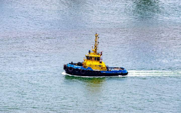 Remorqueur portuaire jaune et bleu naviguant sur une eau calme