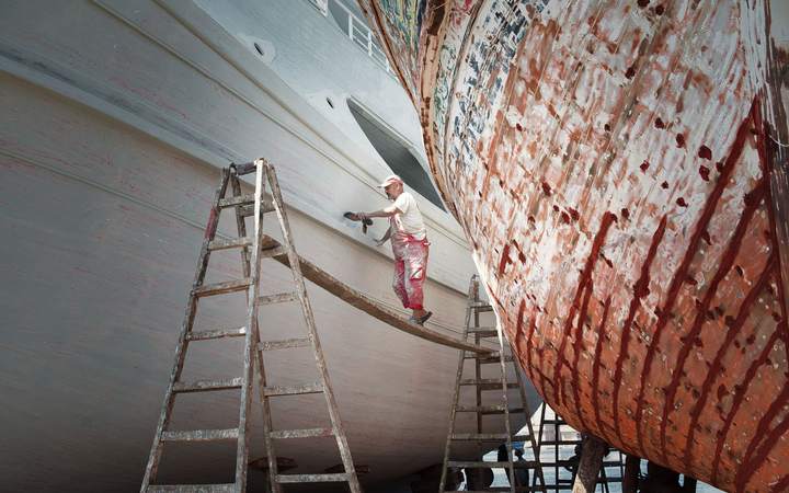 Ouvrier sur une échelle préparant la coque d’un bateau en cale sèche, entre deux navires