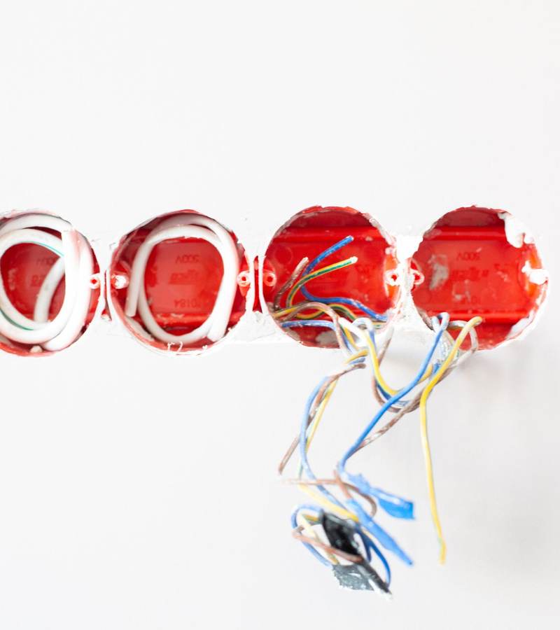 Boîtes d’encastrement rouges posées dans un mur blanc avec fils électriques sortant des boîtiers