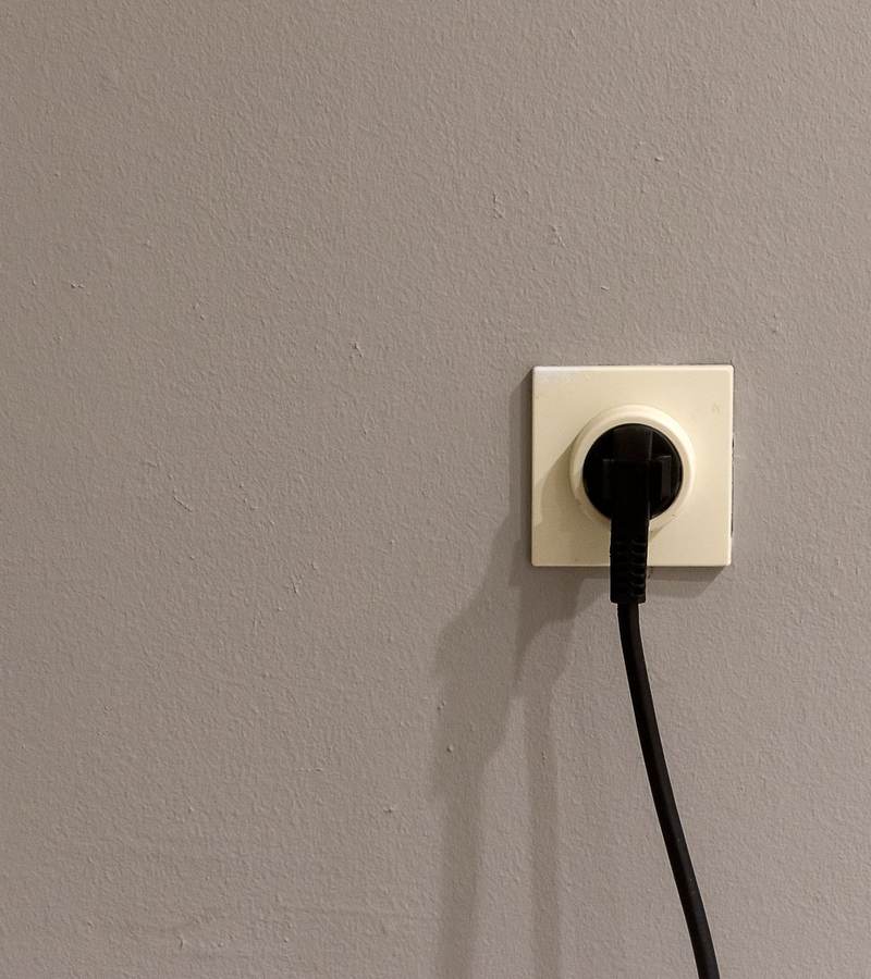 Prise électrique murale avec une fiche branchée et son câble noir sur un mur gris
