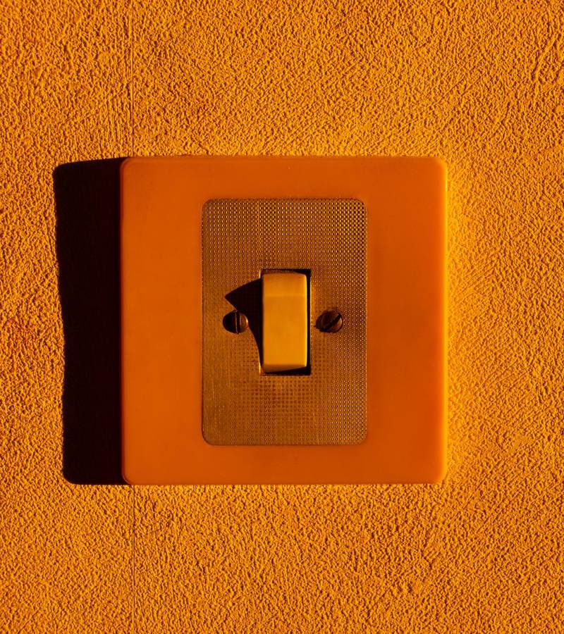 Interrupteur à bascule orange fixé sur un mur crépi de couleur orange