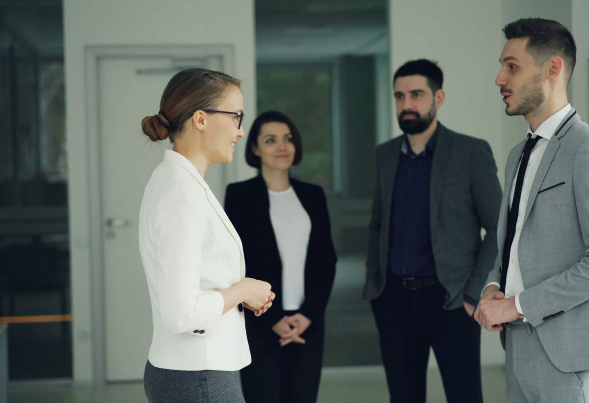 Quatre collègues en tenue professionnelle discutent debout dans un couloir de bureaux