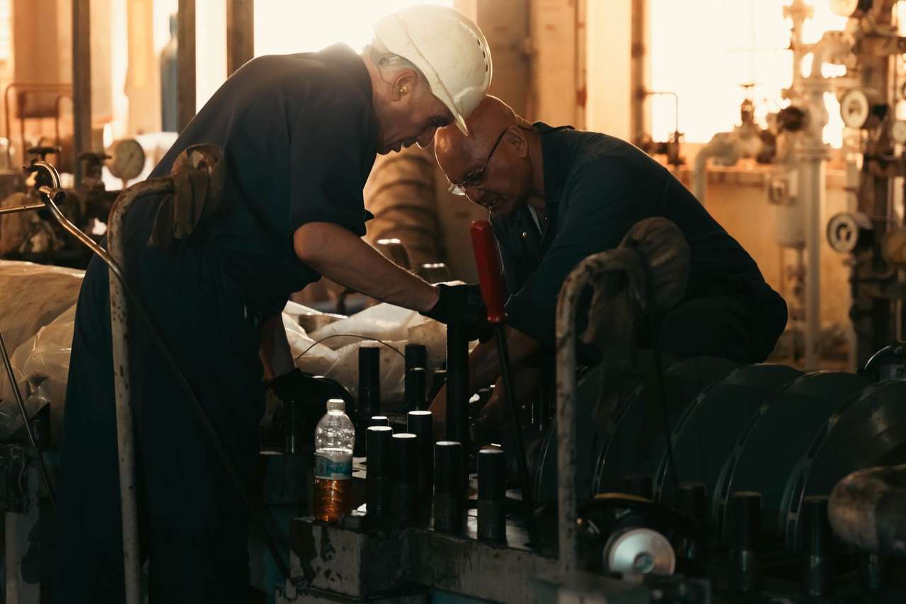 Deux techniciens penchés sur une machine industrielle dans un atelier en contre-jour
