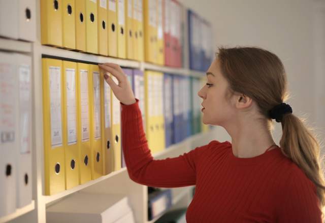 Femme de profil sélectionnant un classeur sur une étagère d’archives