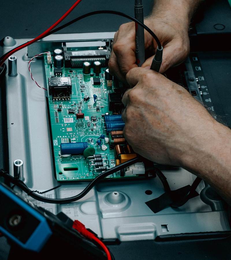 Mains d’un technicien mesurant une carte électronique avec les pointes de touche d’un multimètre