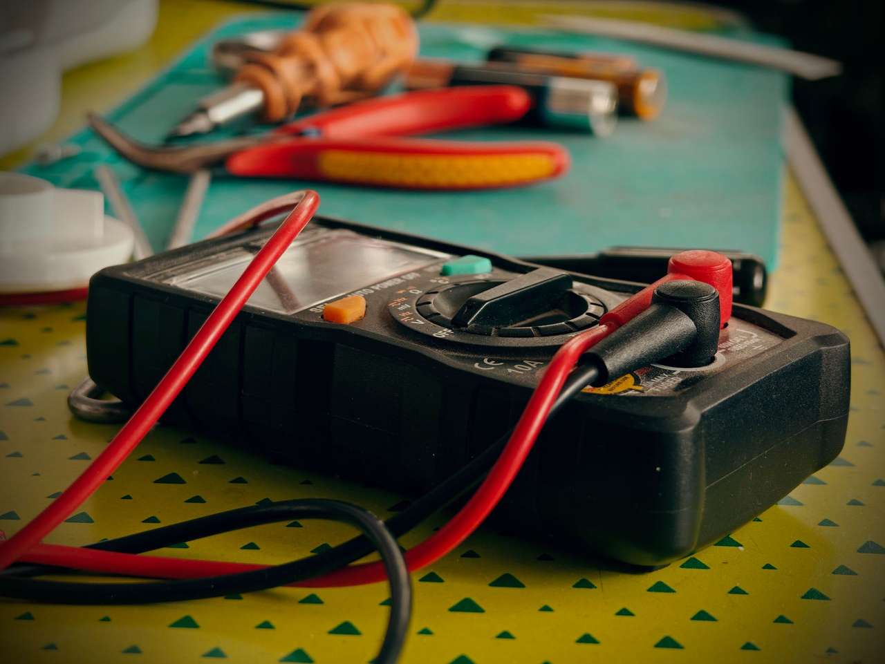 Multimètre avec cordons de mesure rouges et noirs posé sur un établi avec pinces et outils