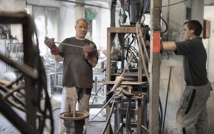 Deux ouvriers en atelier industriel manipulant des pièces métalliques avec des gants de protection