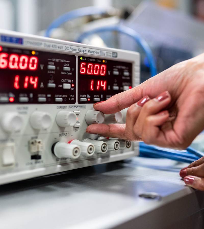Main réglant une alimentation électrique de laboratoire affichant tension et courant
